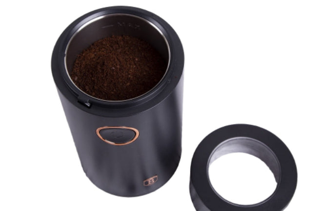 Black coffee grinder with coffee beans on a wooden surface