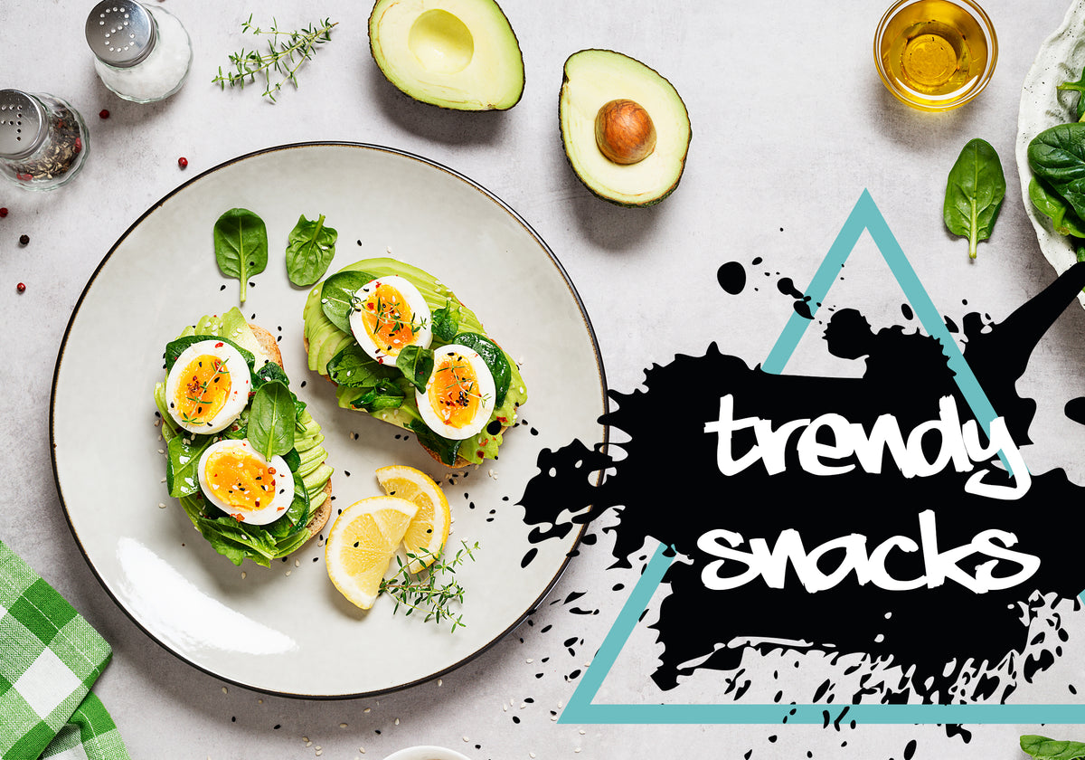 Avocado toast with eggs on a plate, surrounded by avocados, lemon, and herbs, with 'trendy snacks' text.