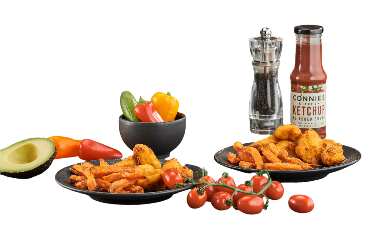 Black air fryer with plates of fried food, vegetables, and a bottle of ketchup on a gray surface.